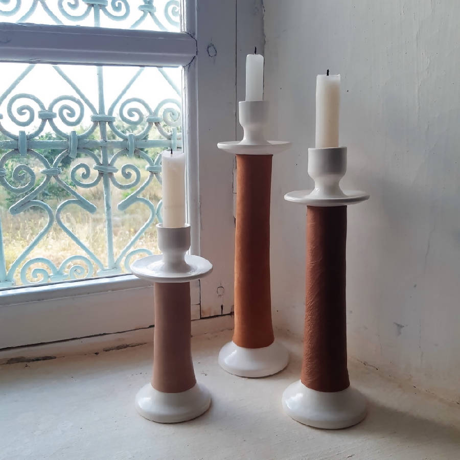Three leather-wrapped candle holders in graduated heights with lit-ready candles at a window