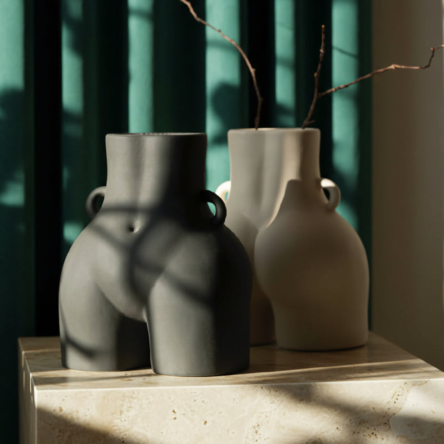 Two Her Vase ceramic vases in stone gray and cream on a stone ledge, a dried branch in one