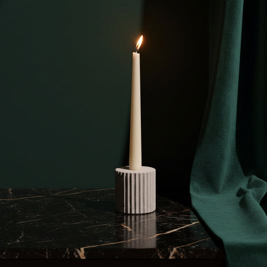 Fluted sandstone Pilar taper holder with a lit ivory candle on a dark marble table