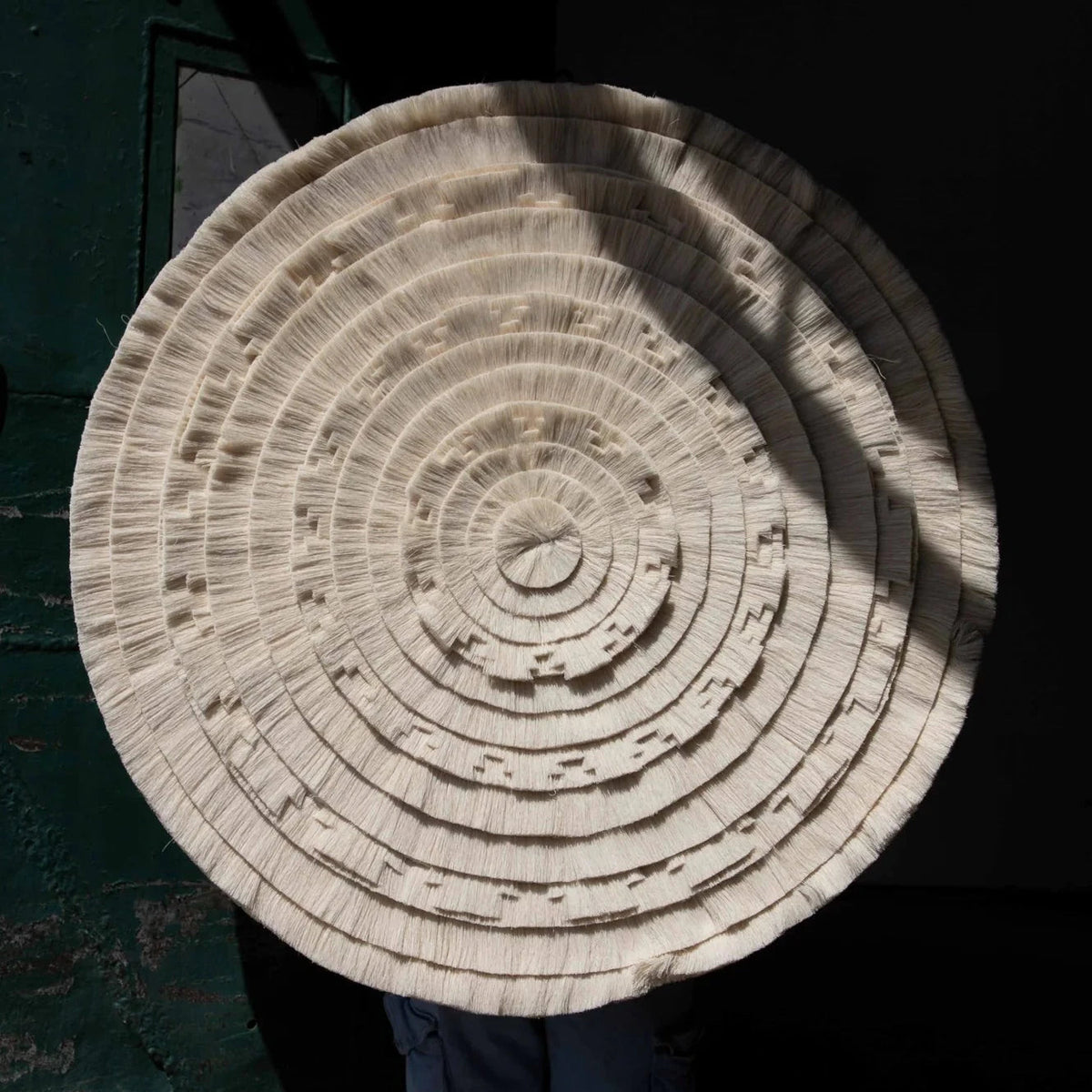 Circular Calendario Azteca cotton tapestry held up against a dark background