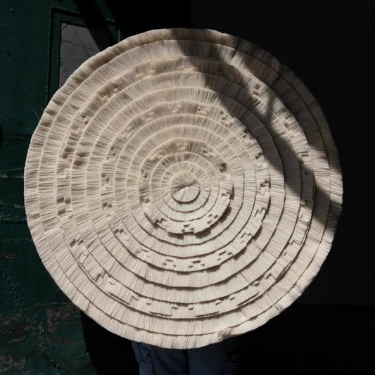 Circular Calendario Azteca cotton tapestry held up against a dark background