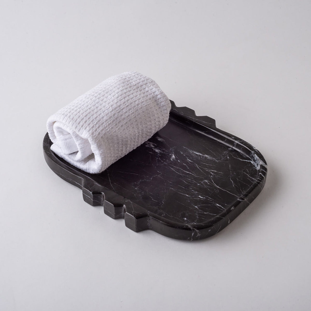 Black marble Tauro tray holding a rolled white towel, seen from above at an angle