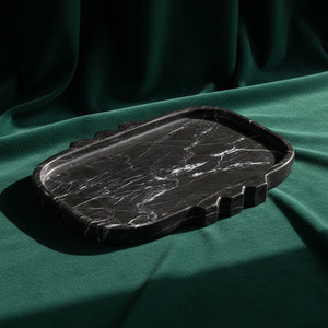 Tauro tray in black marble with white veining and a notched stepped edge, on deep green fabric