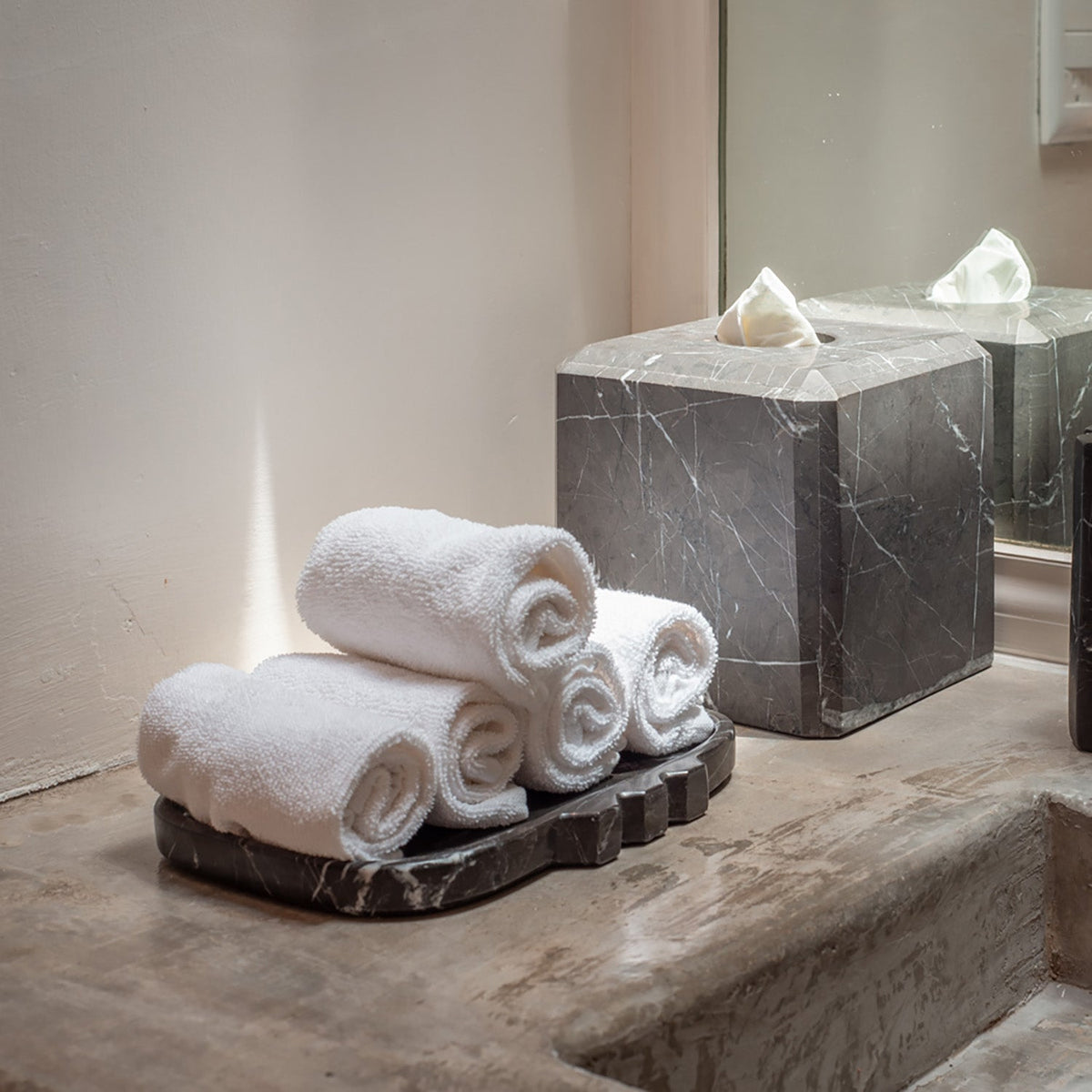 Tauro tray on a bathroom surface with stacked rolled towels beside a gray marble box