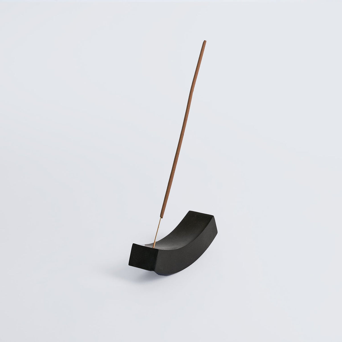 Curved black onyx incense holder on white, holding a single incense stick