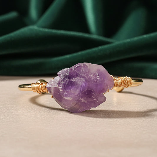Gold cuff with a chunky pale amethyst crystal bound on with coiled gold wire, photographed against green velvet