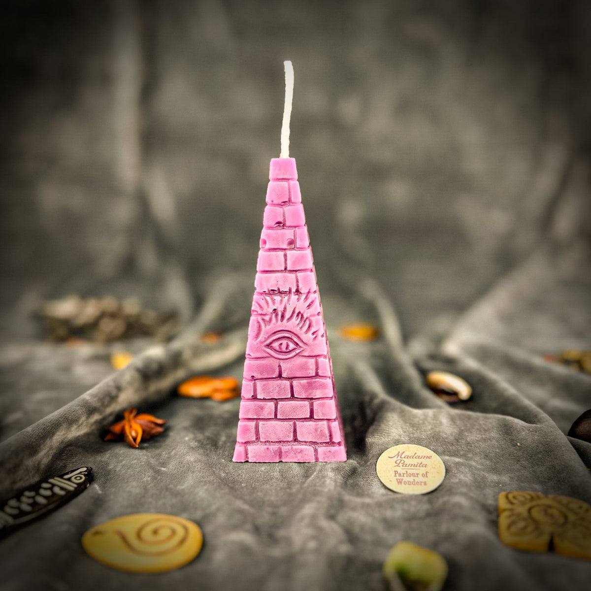 Dusty rose pyramid candle on gray velvet, brick courses running to the wick at the apex.