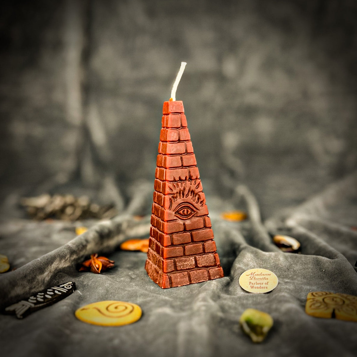 Rust-brown pyramid candle on gray velvet, the eye picked out by side light.