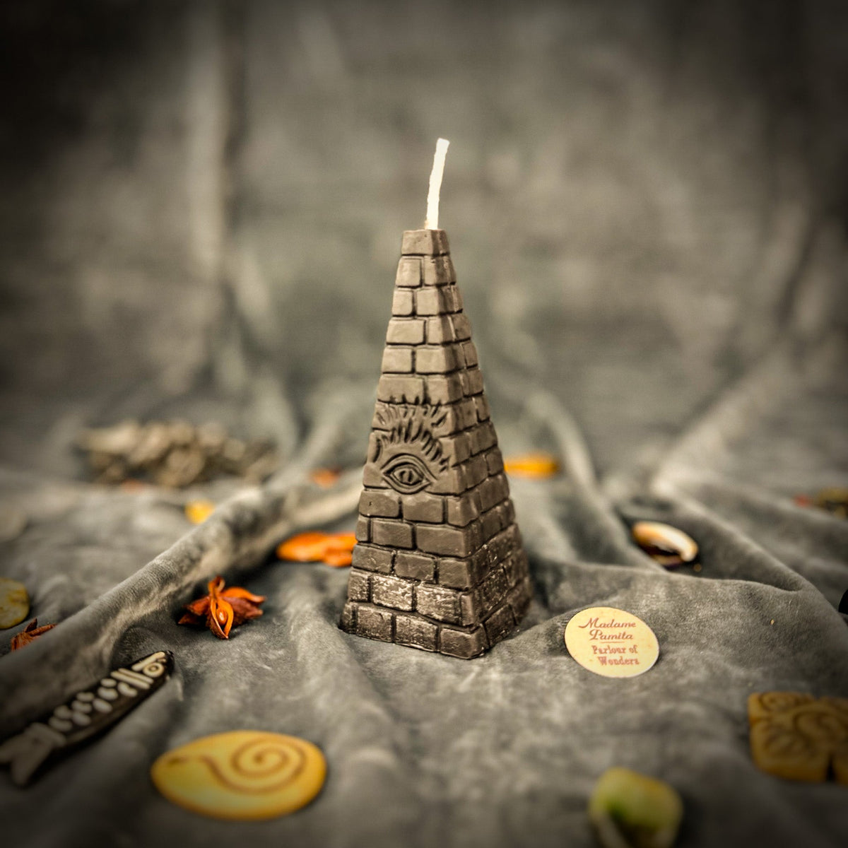 Black pyramid candle on gray velvet, brickwork and eye showing as texture rather than pattern.