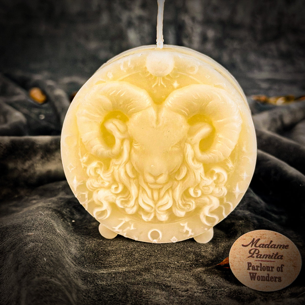 Cream-white Aries medallion candle, the relief readable through its shadows alone.
