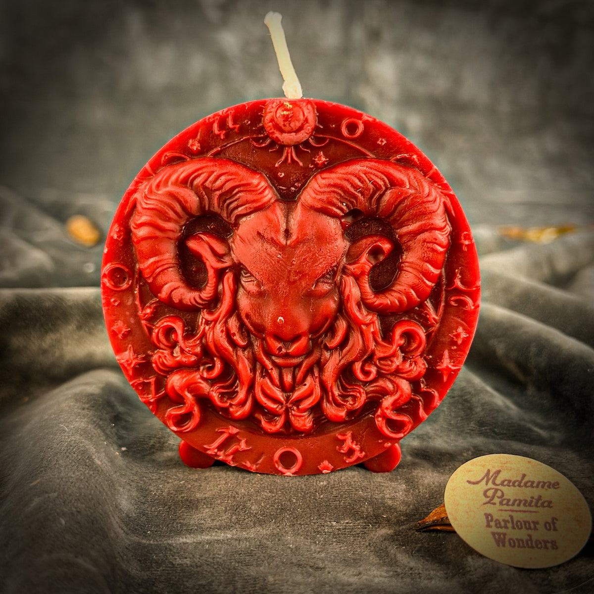 Red Aries medallion candle on gray velvet, the deepest cut of the range.