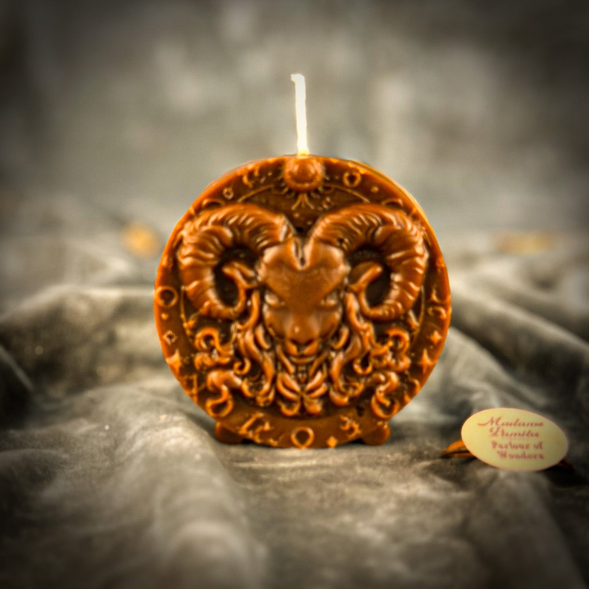 Red-brown Aries medallion candle standing on its small molded feet.