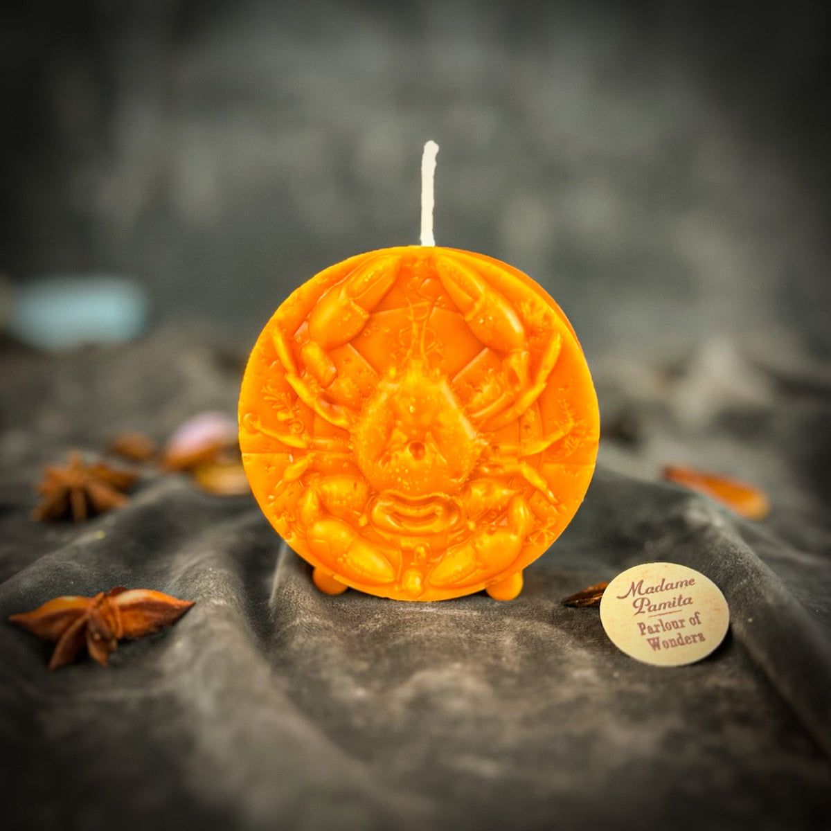 Cancer Crab zodiac spell candle in orange on draped gray fabric