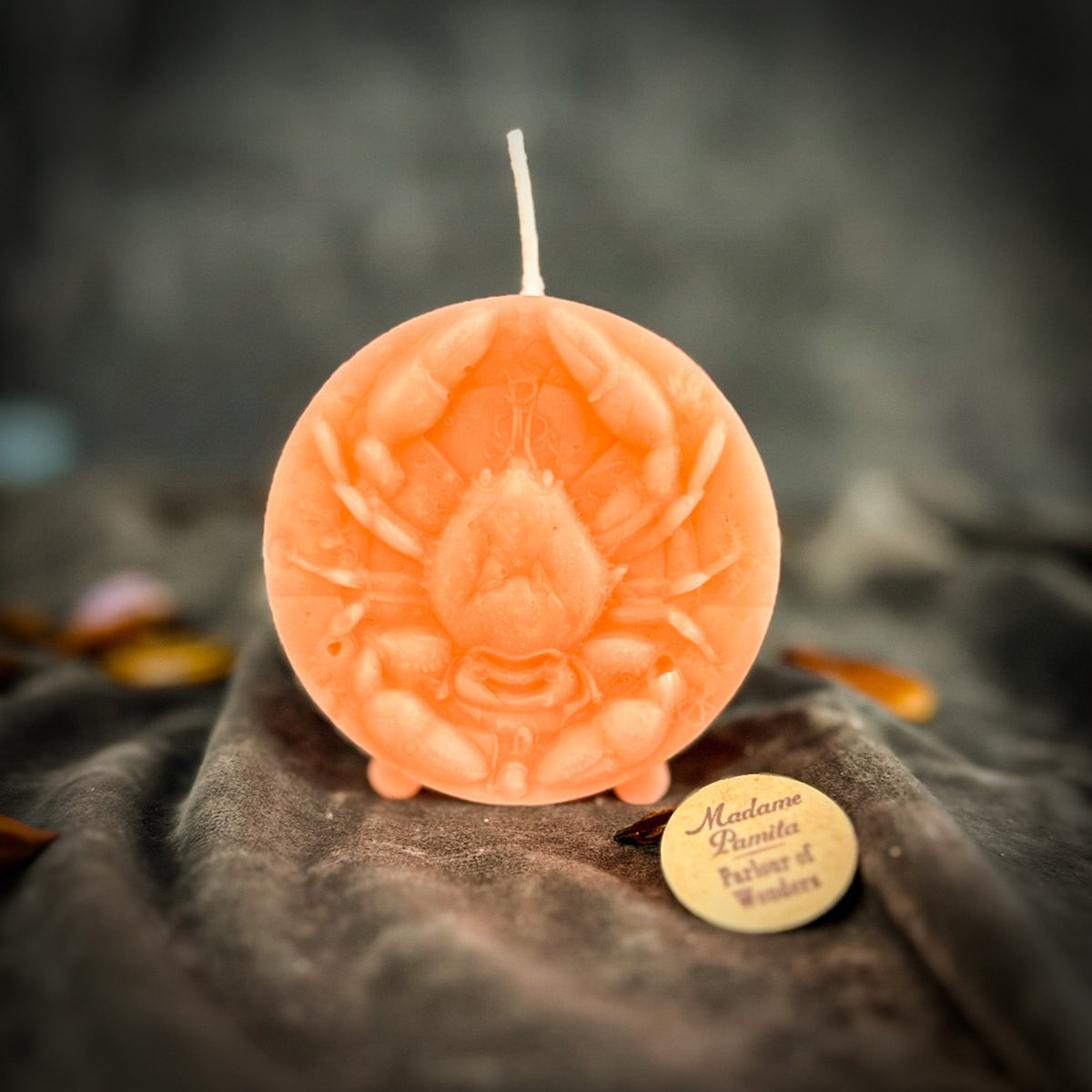 Cancer Crab zodiac spell candle in pink on draped gray fabric