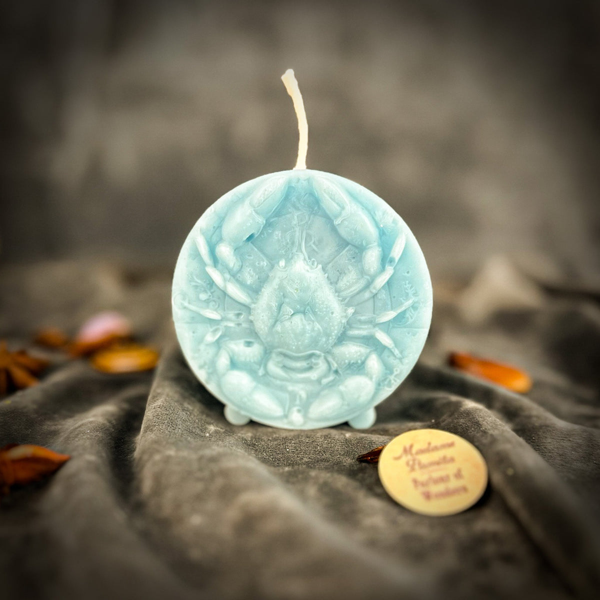 Cancer Crab zodiac spell candle in pale blue on draped gray fabric
