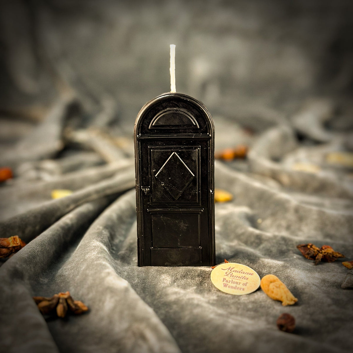 Black door-shaped spell candle on gray velvet, the panel detail catching the light along one edge
