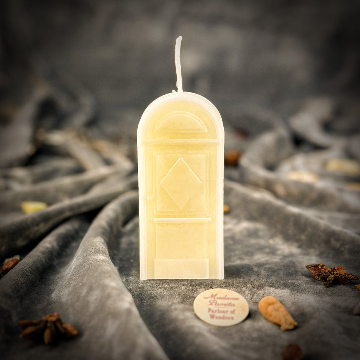 Cream-white door-shaped spell candle on gray velvet, the panelled door and diamond motif picked out in the wax