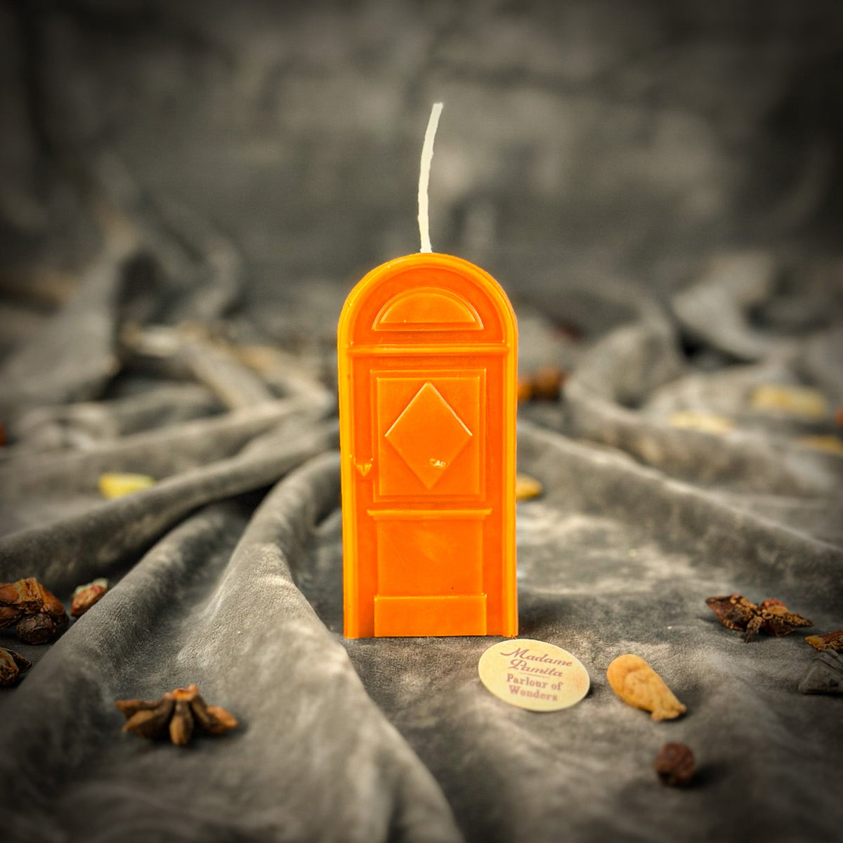 Orange door-shaped spell candle standing on gray velvet with whole spices scattered in the folds