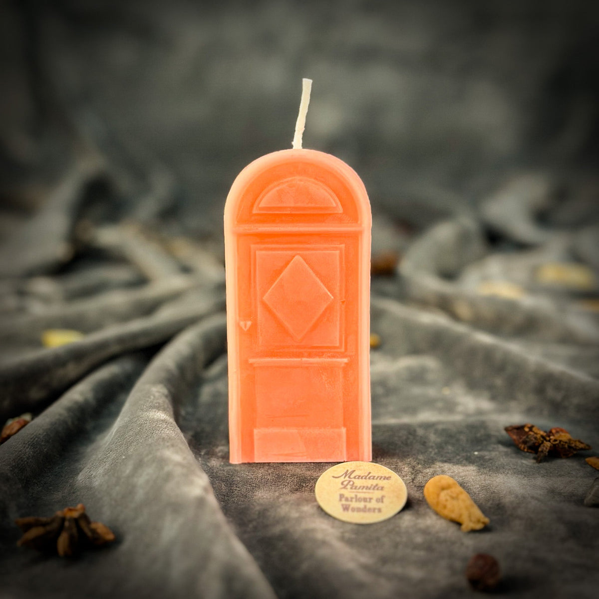 Soft pink door-shaped spell candle on gray velvet with the Parlour of Wonders token in front