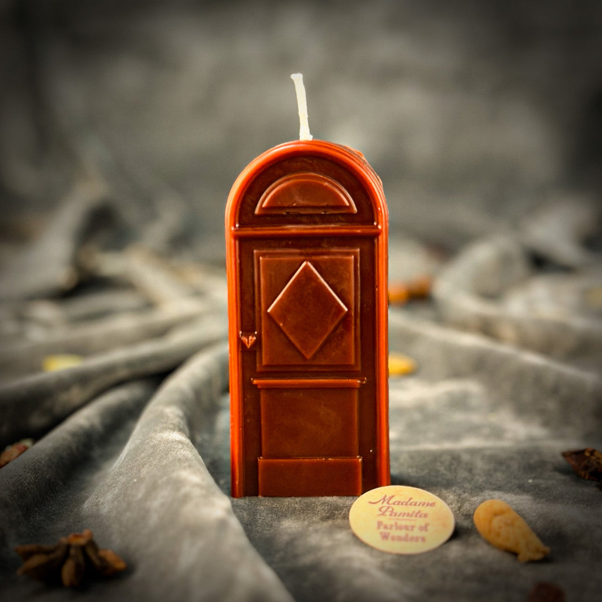 Brown door-shaped spell candle on gray velvet with star anise and dried root pieces around the base