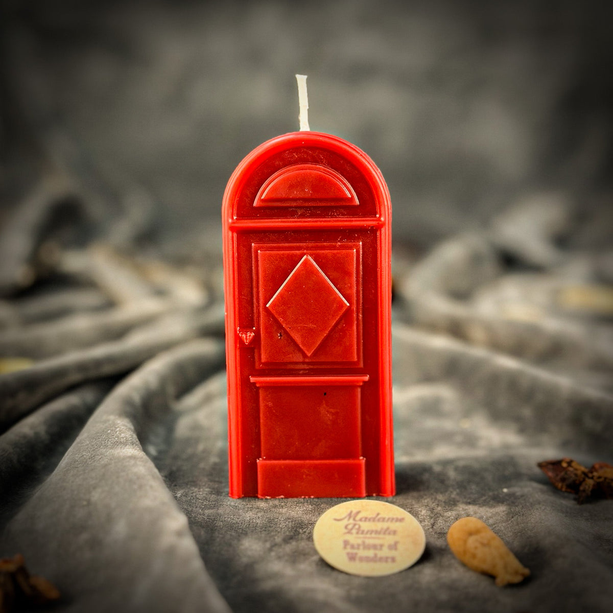 Deep red door-shaped spell candle on gray velvet, its cotton wick standing proud of the arched top