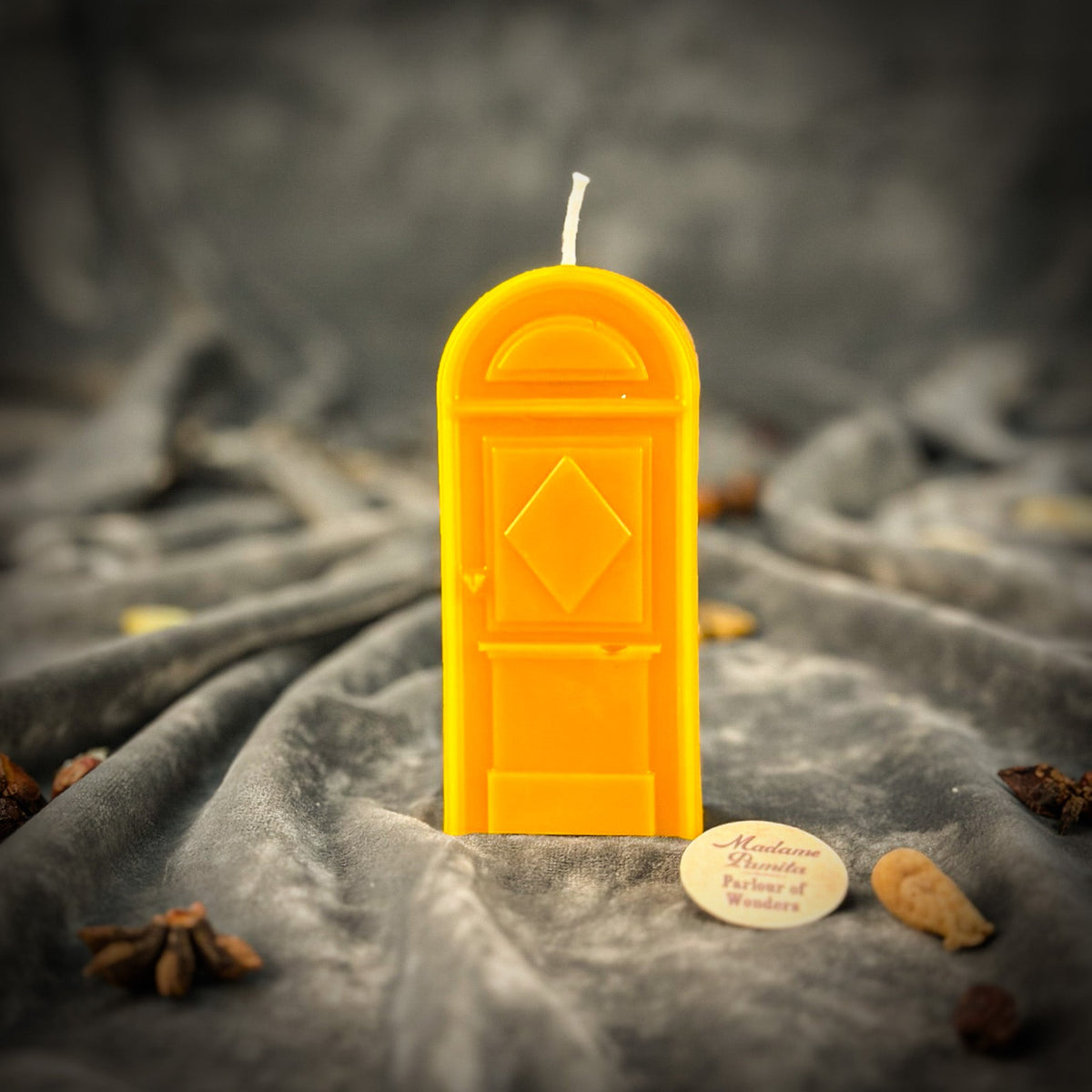 Yellow door-shaped spell candle on gray velvet with the round wooden maker's token resting in front