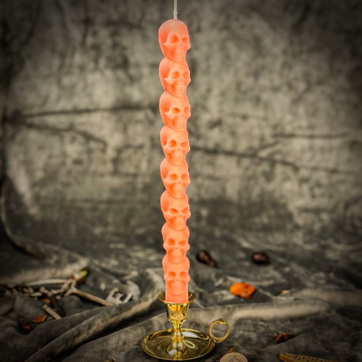 Coral orange beeswax skull taper candle in a brass holder on gray draped fabric