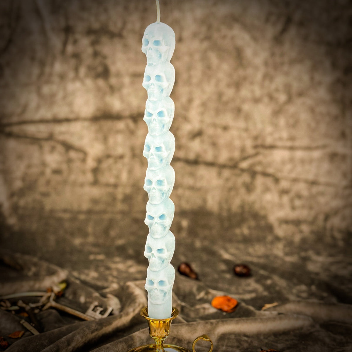 Pale blue beeswax skull taper candle in a brass holder, lit warmly from the side