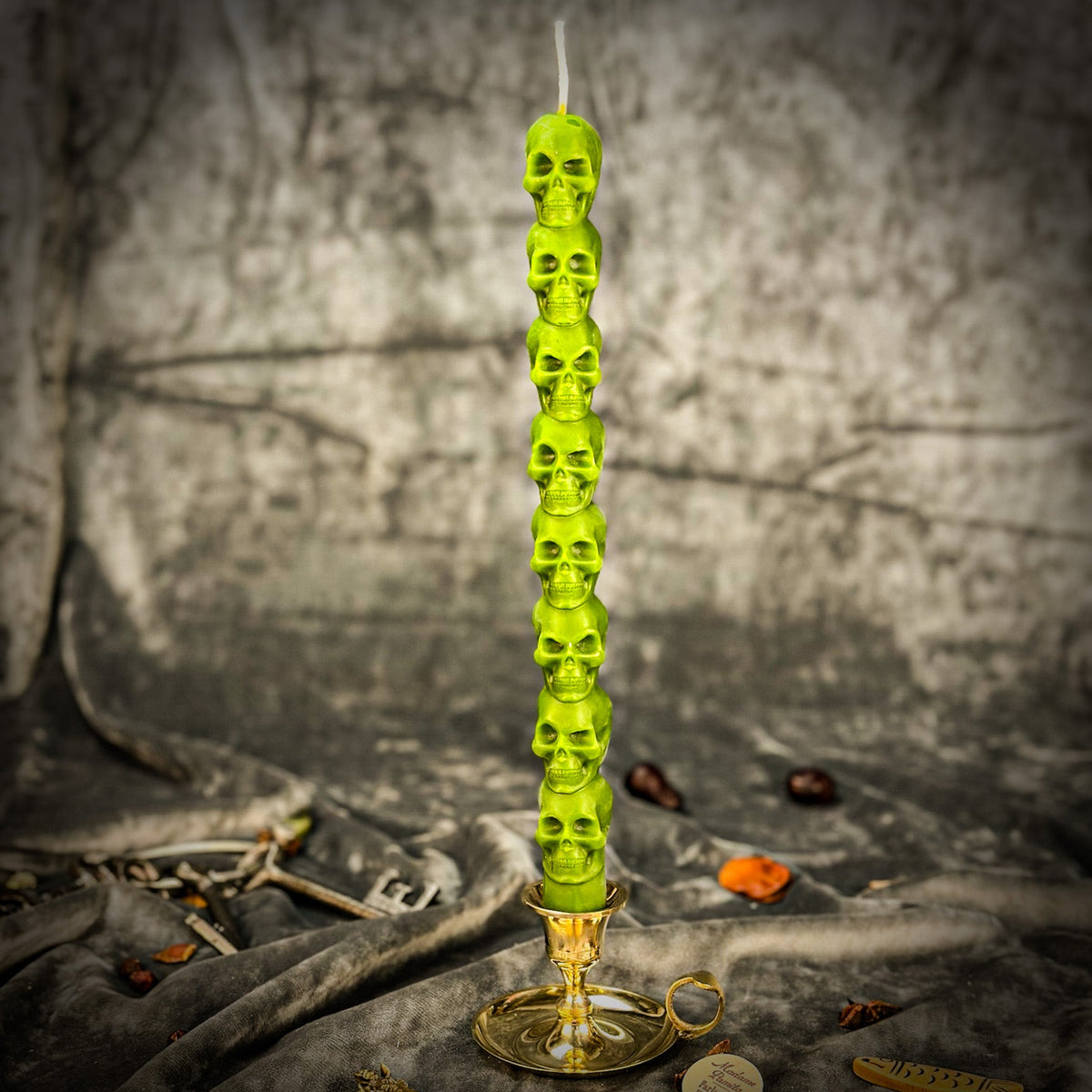 Bright green beeswax skull taper candle in a brass holder on gray draped cloth