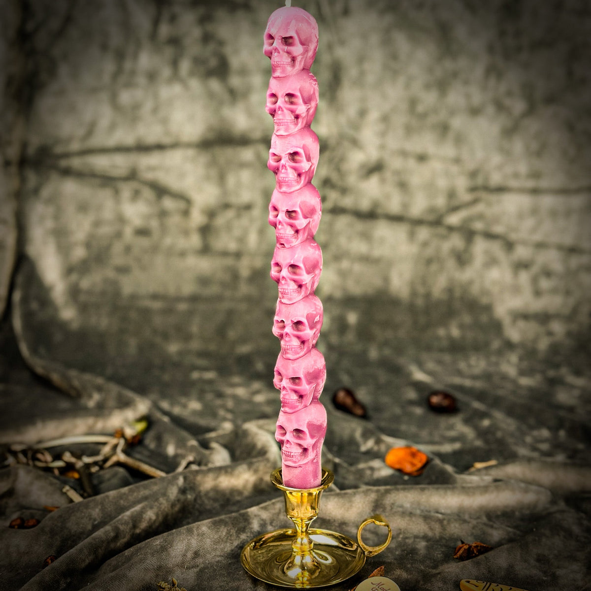 Pink beeswax skull taper candle in a brass holder with scattered dried botanicals