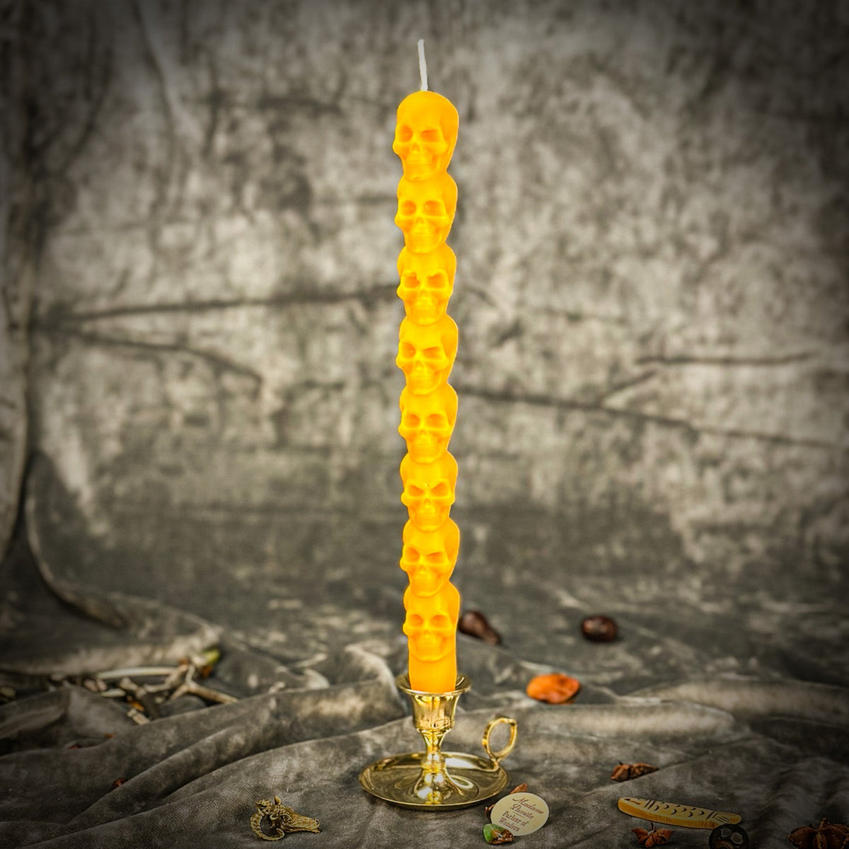 Golden yellow beeswax skull taper candle in a brass holder, each molded skull clearly defined