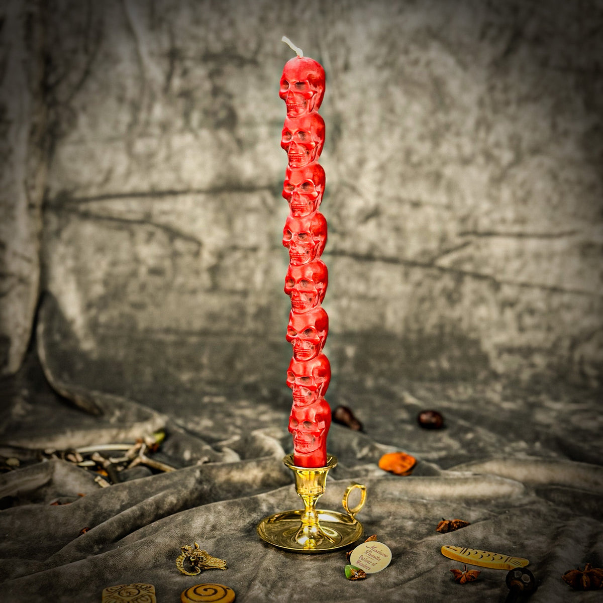 Red beeswax skull taper candle standing in a brass holder against a gray backdrop