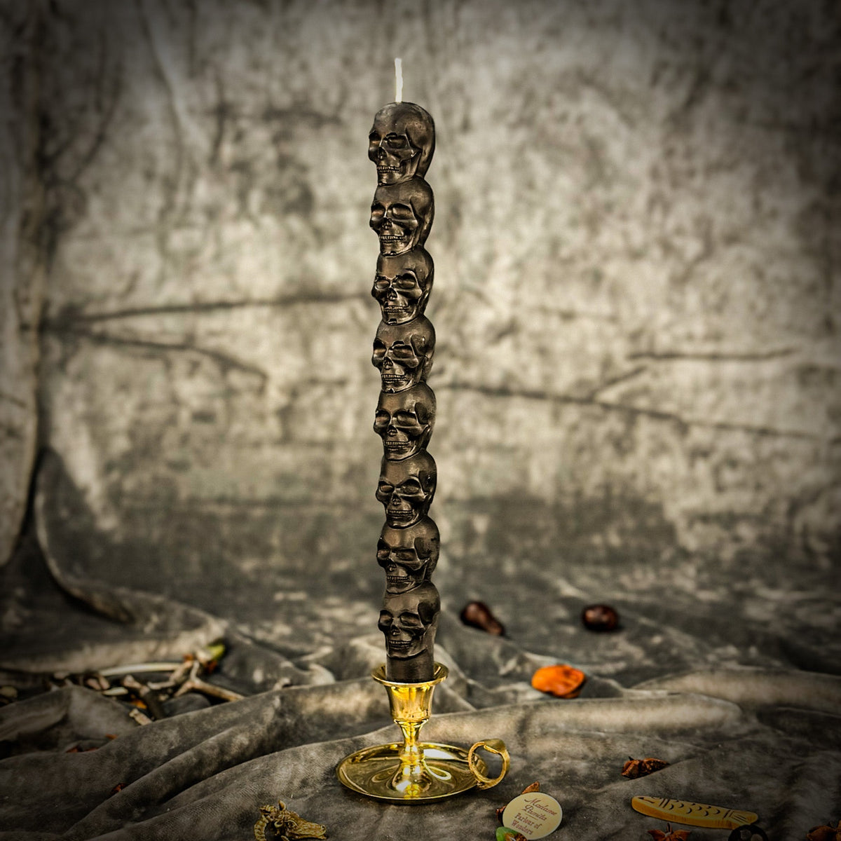Black beeswax skull taper candle in a brass holder on gray cloth