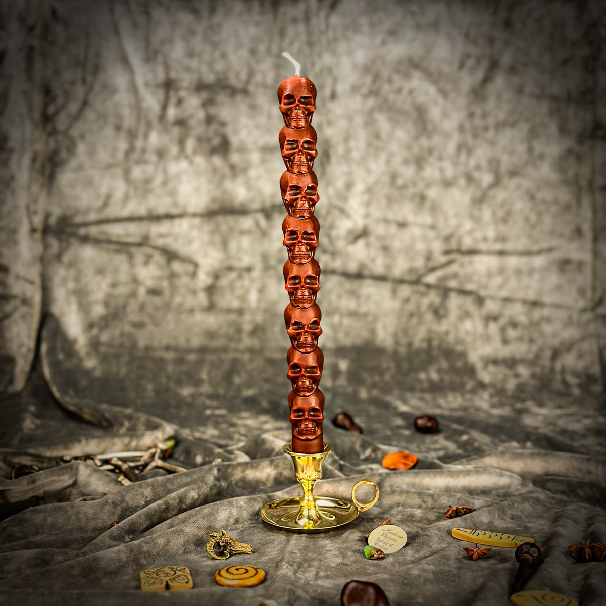 Dark brown beeswax skull taper candle in a brass holder on gray cloth