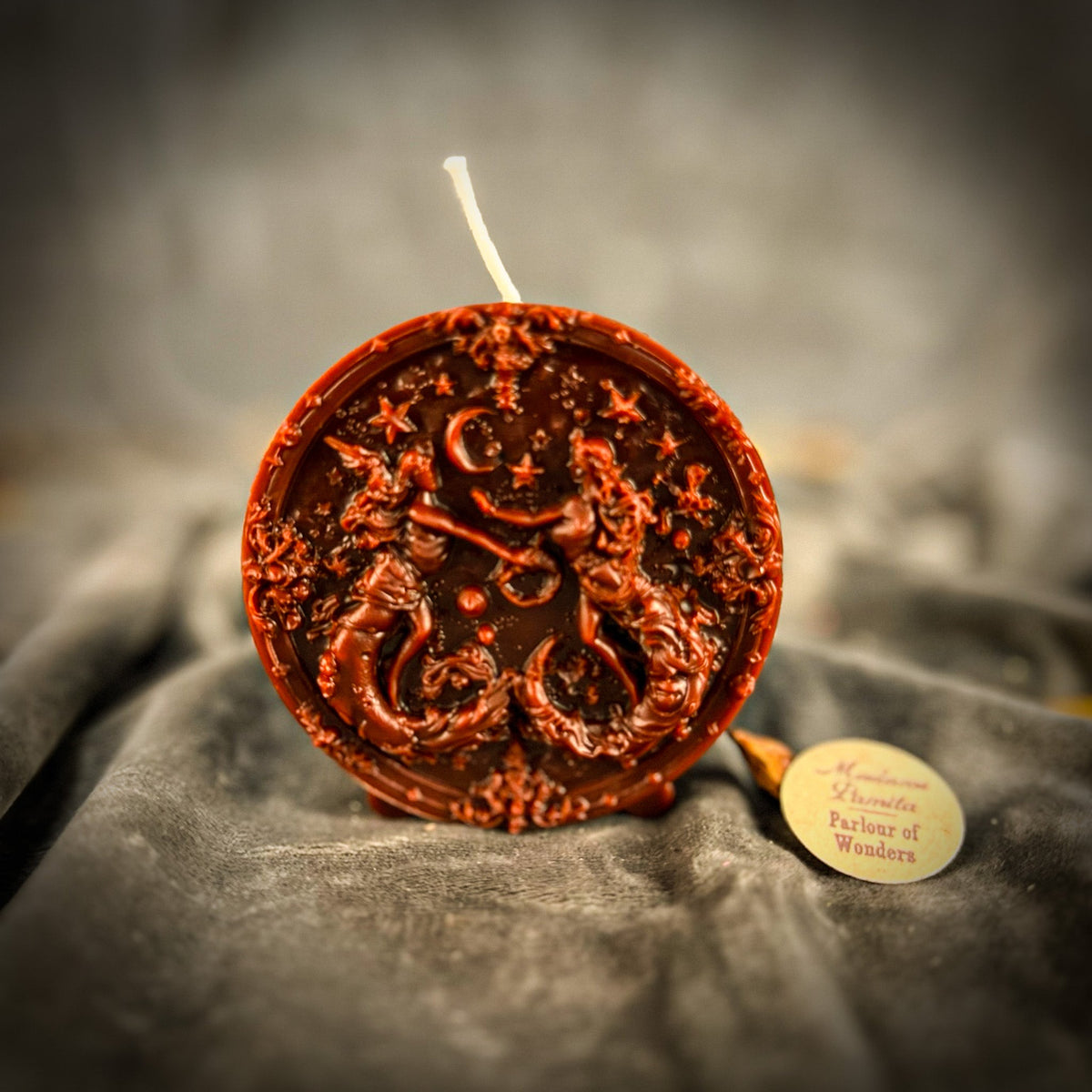 Red-brown Gemini medallion candle on gray velvet, the crescent moon clear at the top.