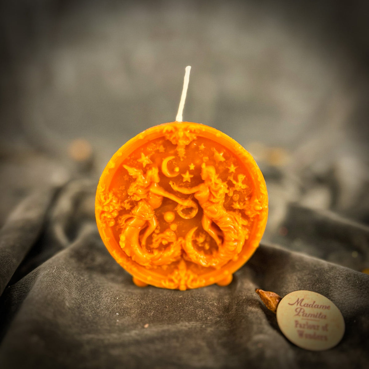 Bright orange Gemini medallion candle, the twins mirrored either side of the glyph.