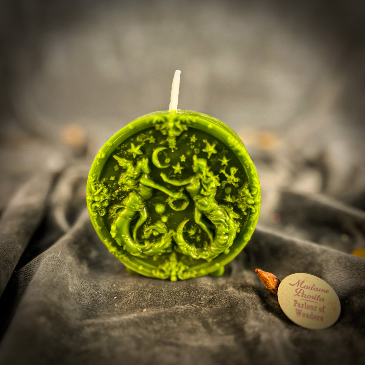 Olive-green Gemini medallion candle standing on its small molded feet.