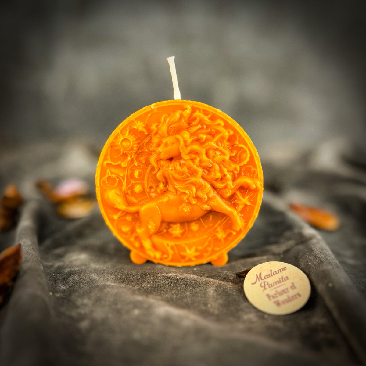 Leo Lion zodiac spell candle in orange on draped gray fabric