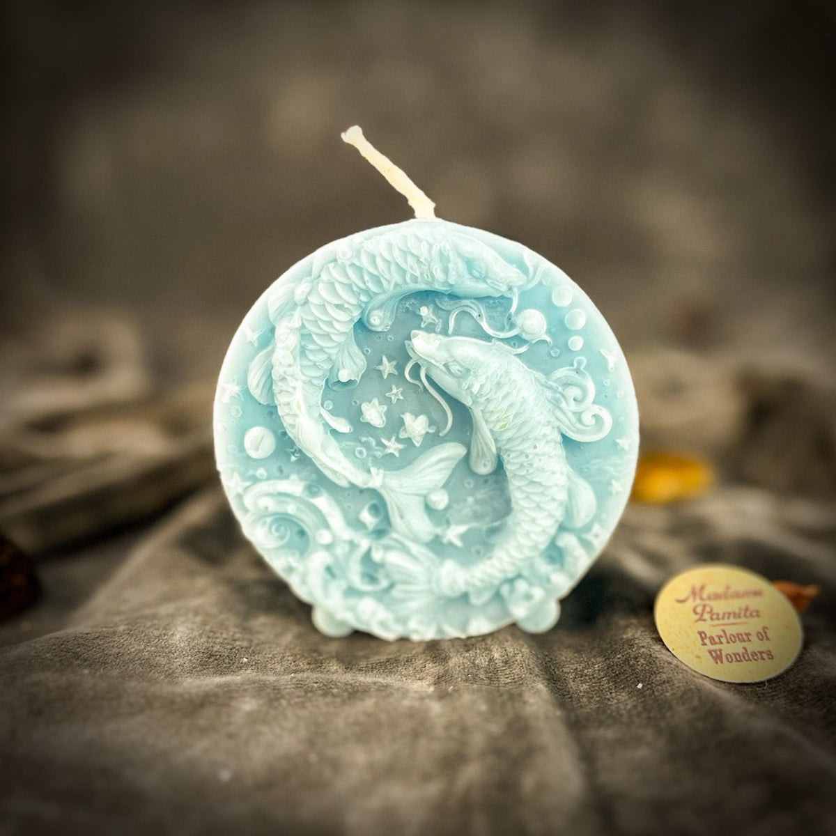 Pale blue Pisces medallion candle, the fish lighter than the field behind them.