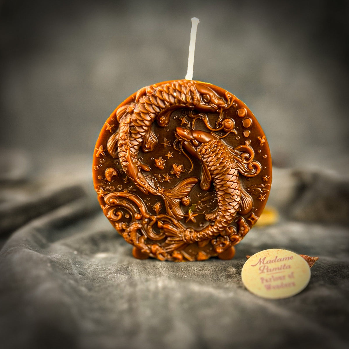 Red-brown Pisces medallion candle, the scrollwork catching a warm side light.