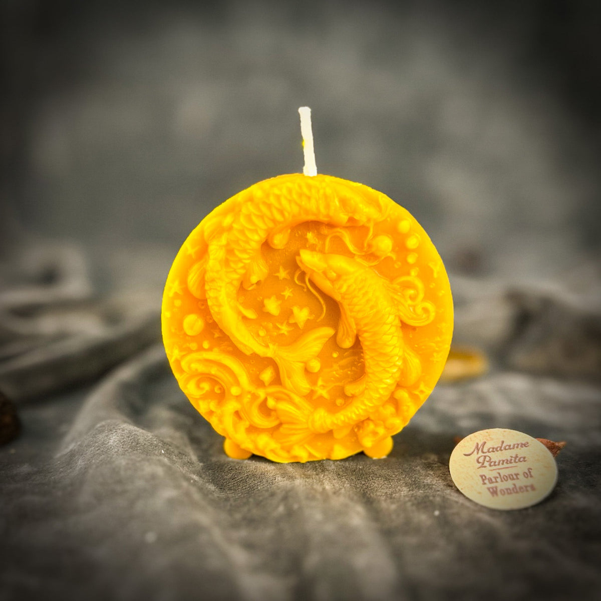 Golden-yellow Pisces medallion candle, translucent where the light passes through.