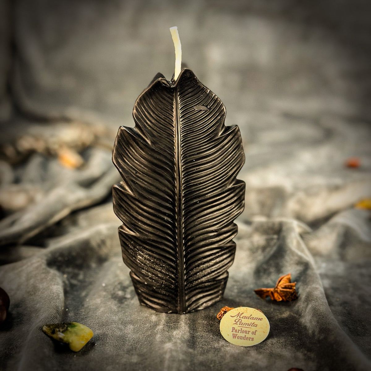 Black leaf-shaped candle standing on gray velvet, the deep vein channels catching the light