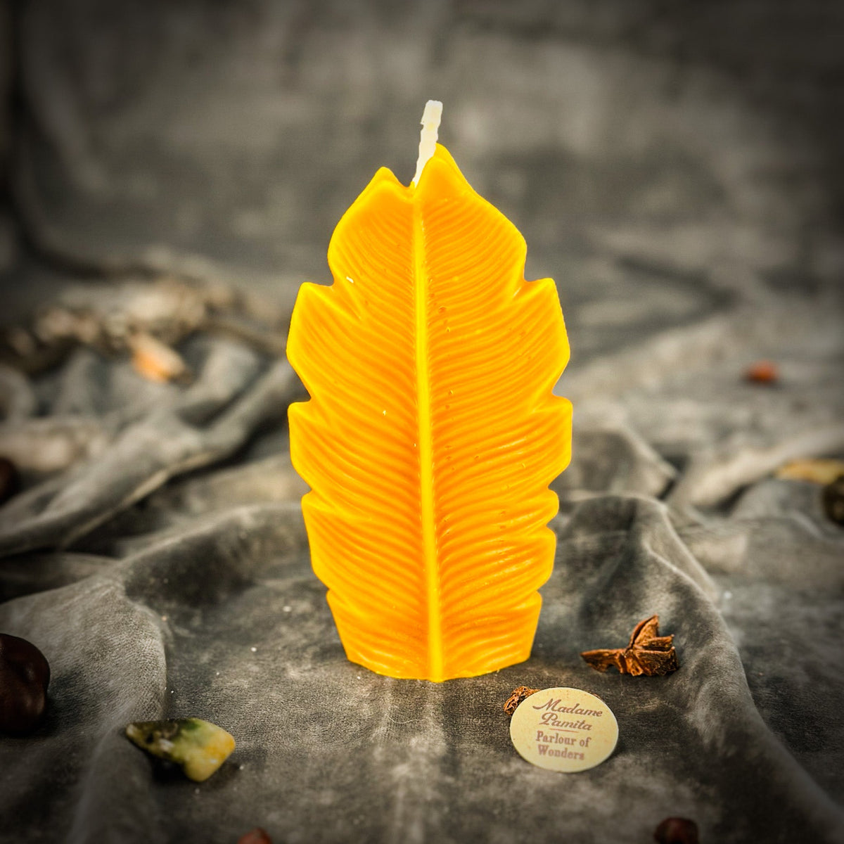 Golden yellow leaf-shaped candle on gray velvet with whole spices scattered in the folds