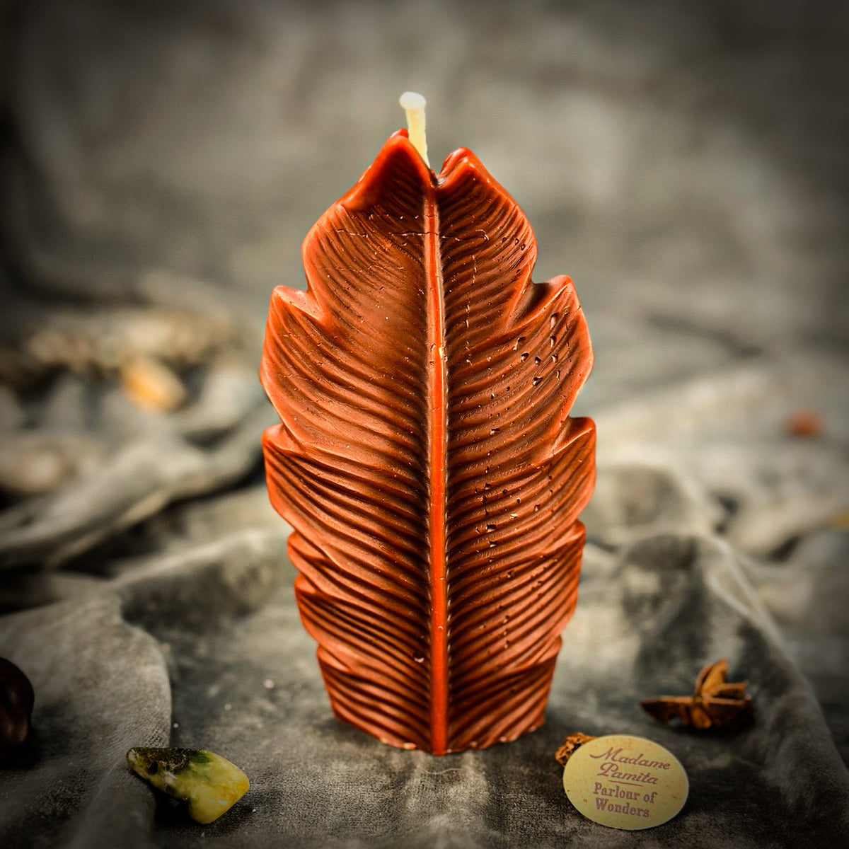 Rust-brown leaf-shaped candle on gray velvet with a green stone and star anise at its base