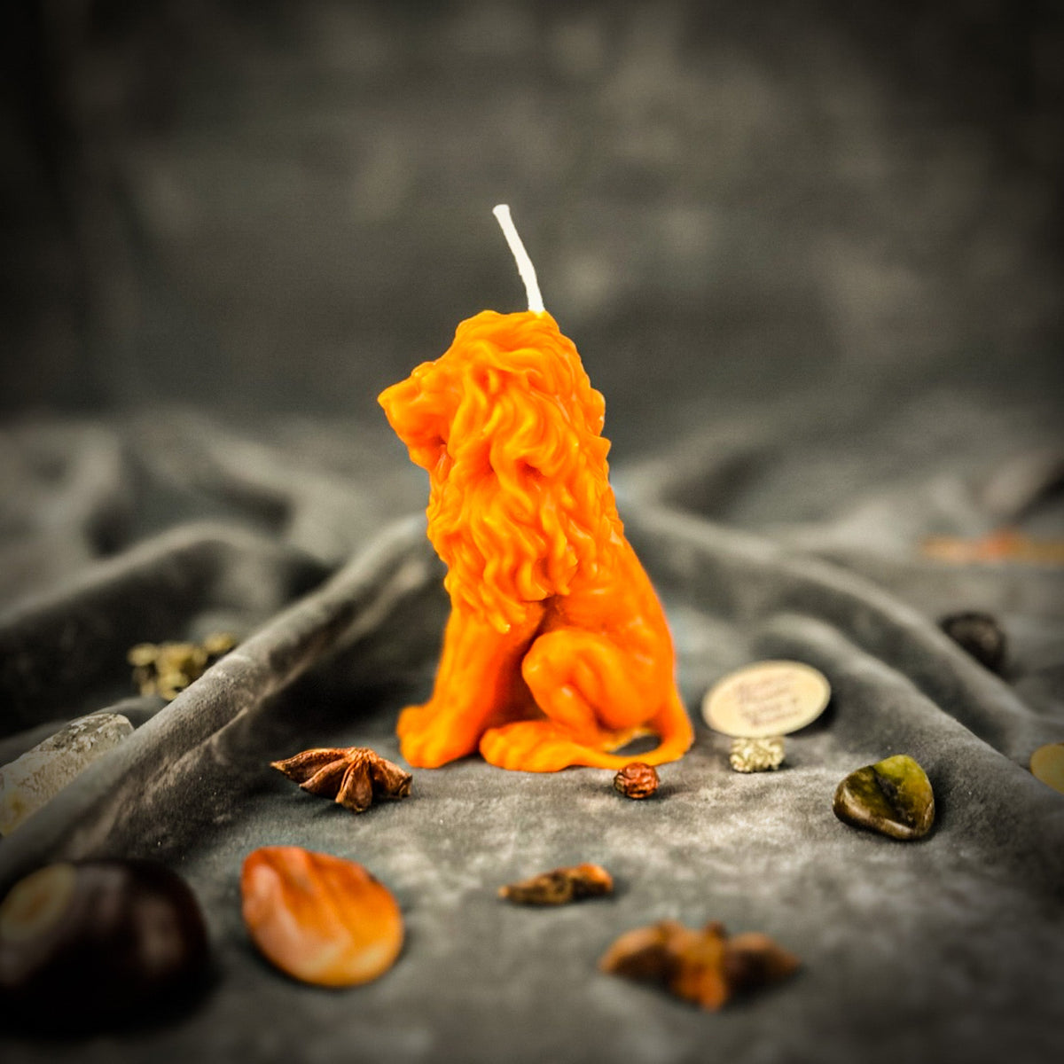 Proud Lion beeswax candle in orange on draped gray fabric