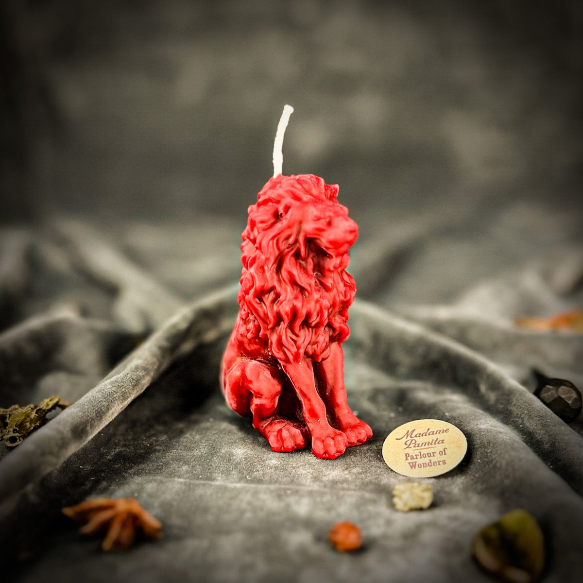 Proud Lion beeswax candle in red on draped gray fabric