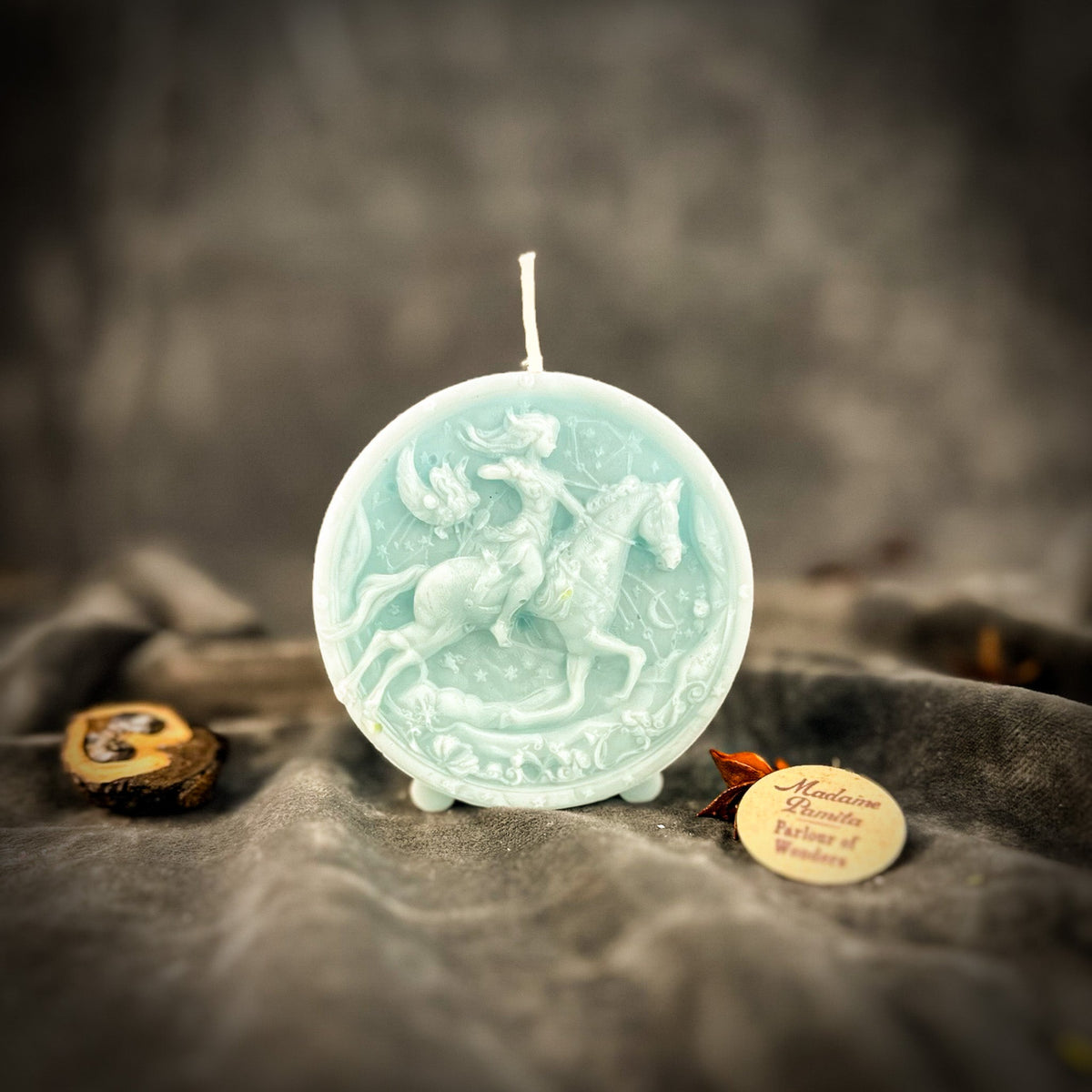 Sagittarius Archer zodiac spell candle in pale blue on draped gray fabric