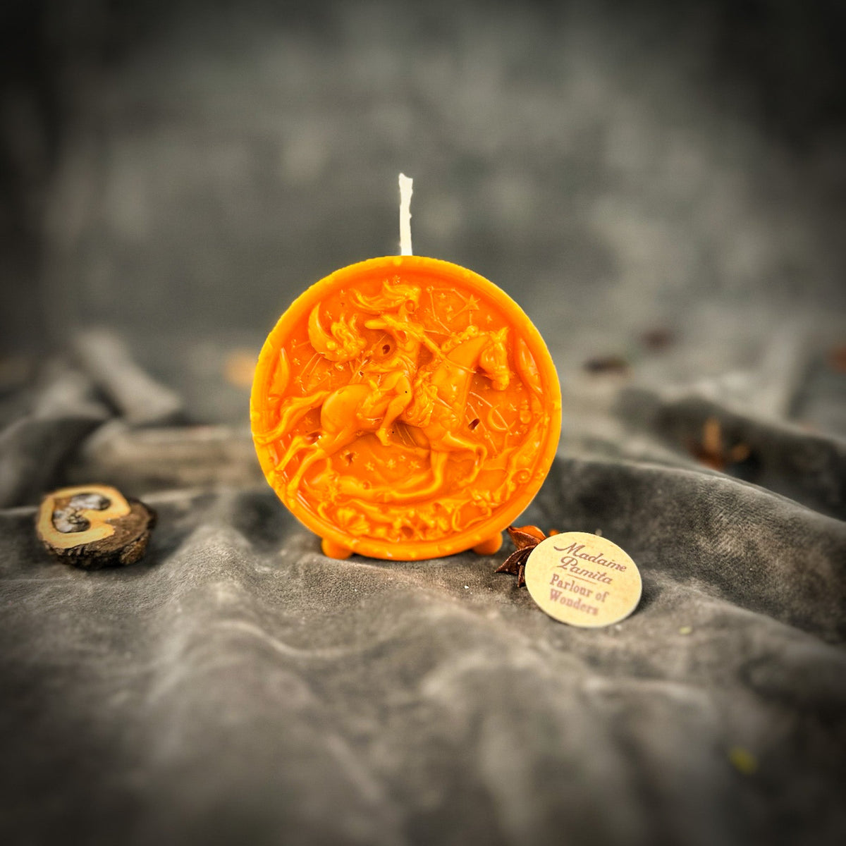 Sagittarius Archer zodiac spell candle in orange on draped gray fabric