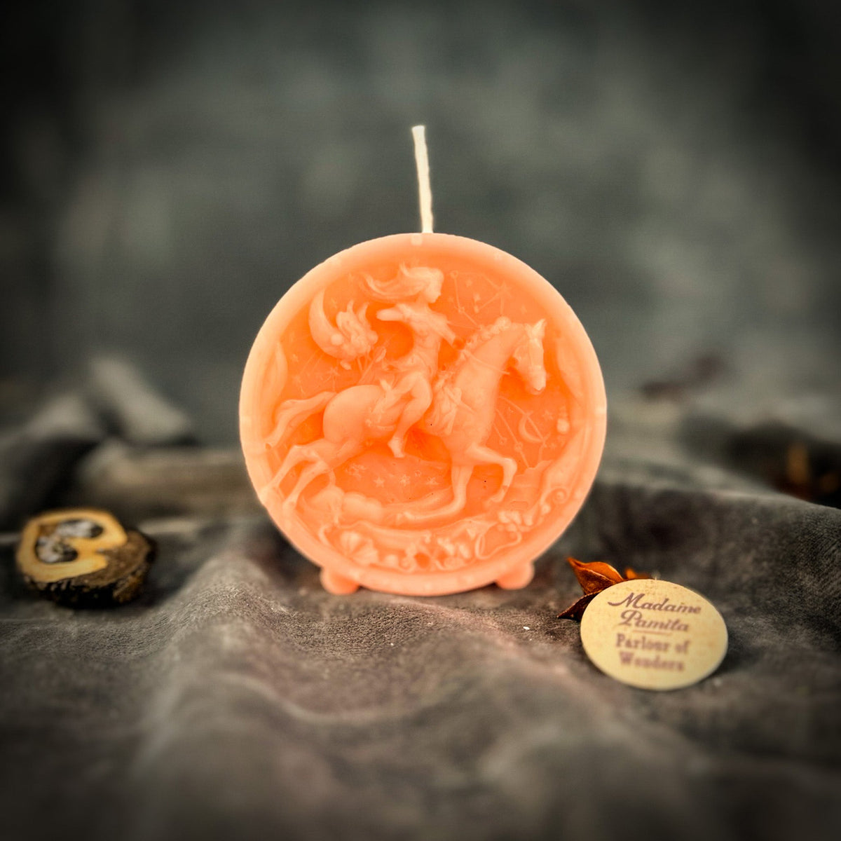 Sagittarius Archer zodiac spell candle in pink on draped gray fabric