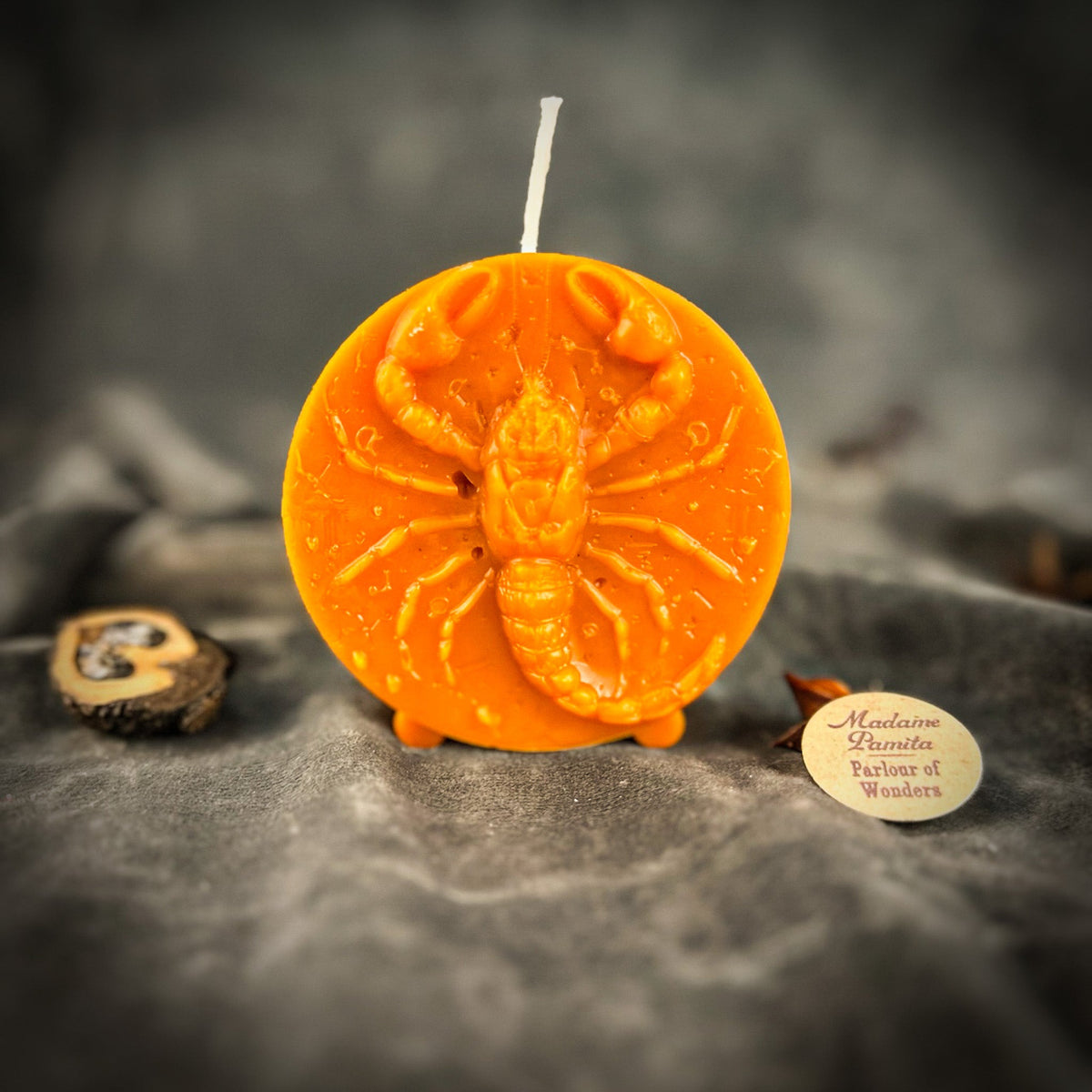 Orange Scorpio medallion candle, the scorpion's claws raised toward the wick.